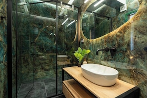 Un baño moderno con cabina de ducha de vidrio, tocador de madera y salpicadero de mármol.