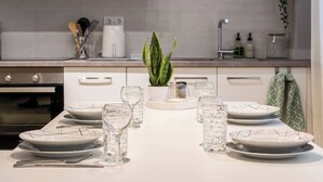 Une cuisine avec une table à manger dressée pour six personnes, une machine à café, une plante et des ustensiles de cuisine.
