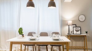 Un coin repas comprenant une table en bois, deux chaises, un banc, des luminaires suspendus, une horloge et une petite table sur laquelle se trouvent une lampe et une plante.