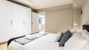 Une chambre moderne avec un grand lit, du linge de lit blanc, une table de chevet et une armoire.
