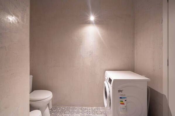 A small, compact bathroom with a toilet, washing machine, and a tiled floor.