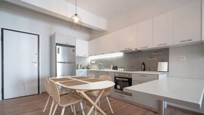 A modern kitchen with white cabinetry, a dining table with chairs, a built-in oven, and a hanging light fixture. - Exclusive Apt In The  Of Athens'_2BD+2 Bathrooms (Athens)