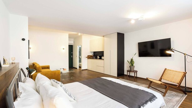 A modern hotel room with a bed, a desk, a chair, a TV, and a kitchen area. - Athens' Best Location~ Unique Magnificent Studio (Athens)