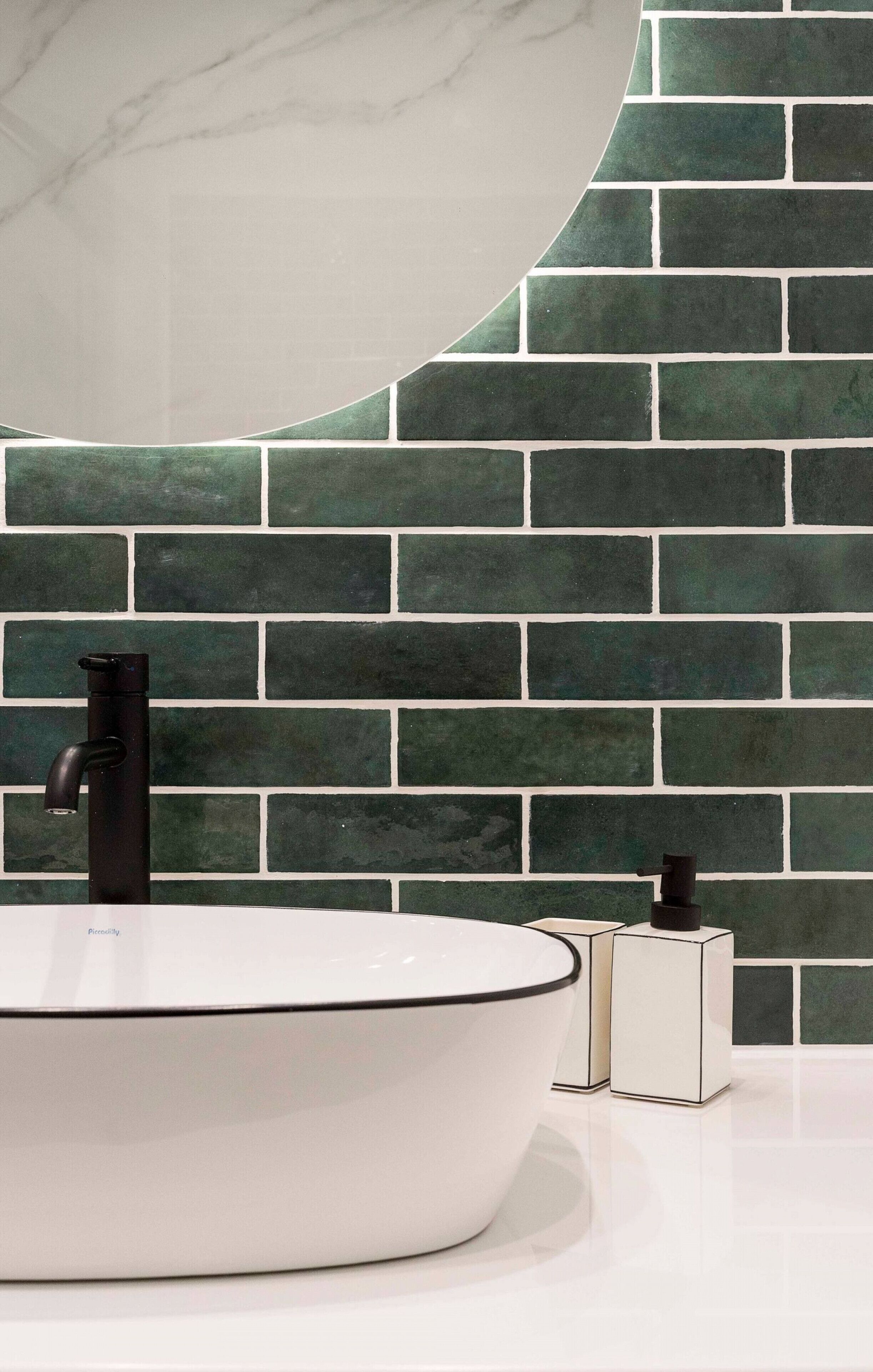 Un baño con lavamanos blanco, grifo negro y pared con azulejos verdes.