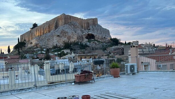 A rooftop terrace with a view of a historic stone fortress, potted plants, and a wooden bench. - 1BR In Plaka | Rooftop Access w/ Acropolis View (Athens)