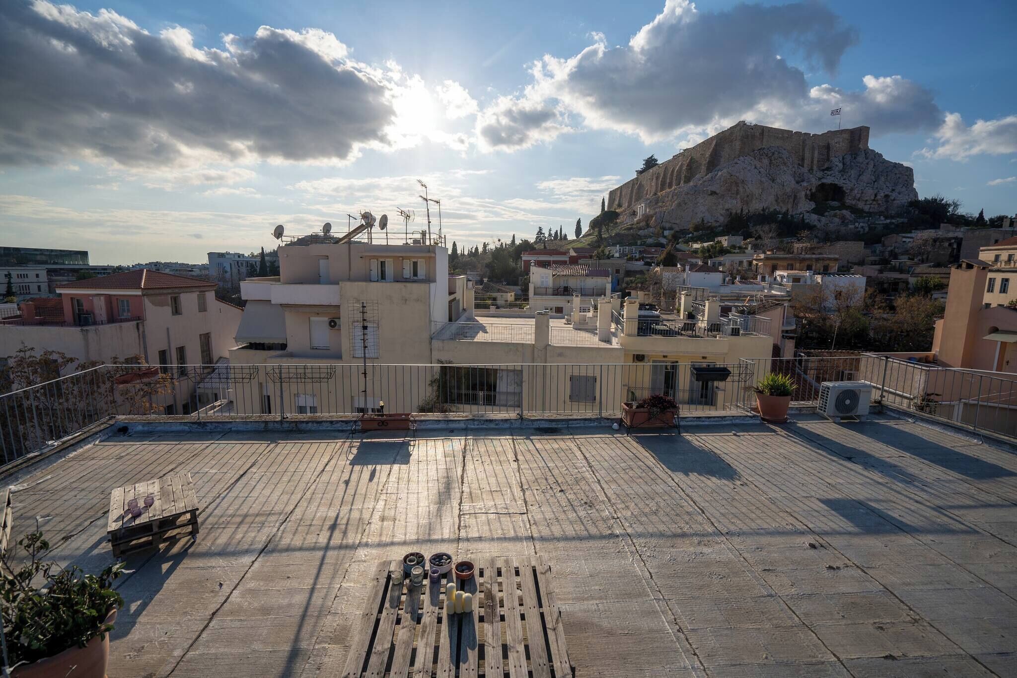 A rooftop terrace with potted plants, a wooden table, and a view of a historic hill with ruins.
