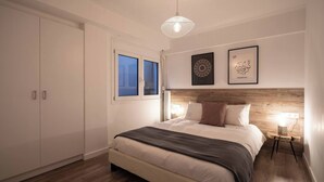 A bedroom with a bed, a window, a wooden headboard, and wall art. - 1BR In Plaka | Rooftop Access w/ Acropolis View (Athens)