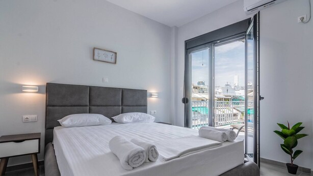 Un dormitorio moderno con una cama grande, una mesita de noche, una planta en maceta y vistas de la ciudad a través de una puerta corrediza de vidrio.
