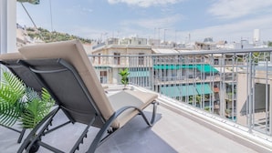 Un balcón con una silla, una planta en maceta y vistas a un paisaje urbano.