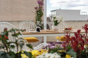 Un tavolo da pranzo con sedie, una caffettiera, un vaso con fiori e un piatto di cibo su un balcone.