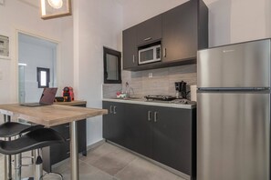 A modern kitchen with dark cabinets, a stainless steel refrigerator, a microwave, and a coffee machine. There is a wooden table with a laptop and a red kettle.