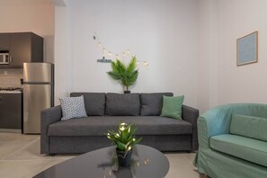 En moderne stue med en grå sofa, en grøn lænestol, et lille rundt bord, en potteplante og en lyskæde på væggen.
