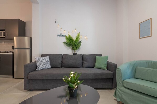 A modern living room with a grey sofa, a green armchair, a small round table, a potted plant, and a string of lights on the wall.