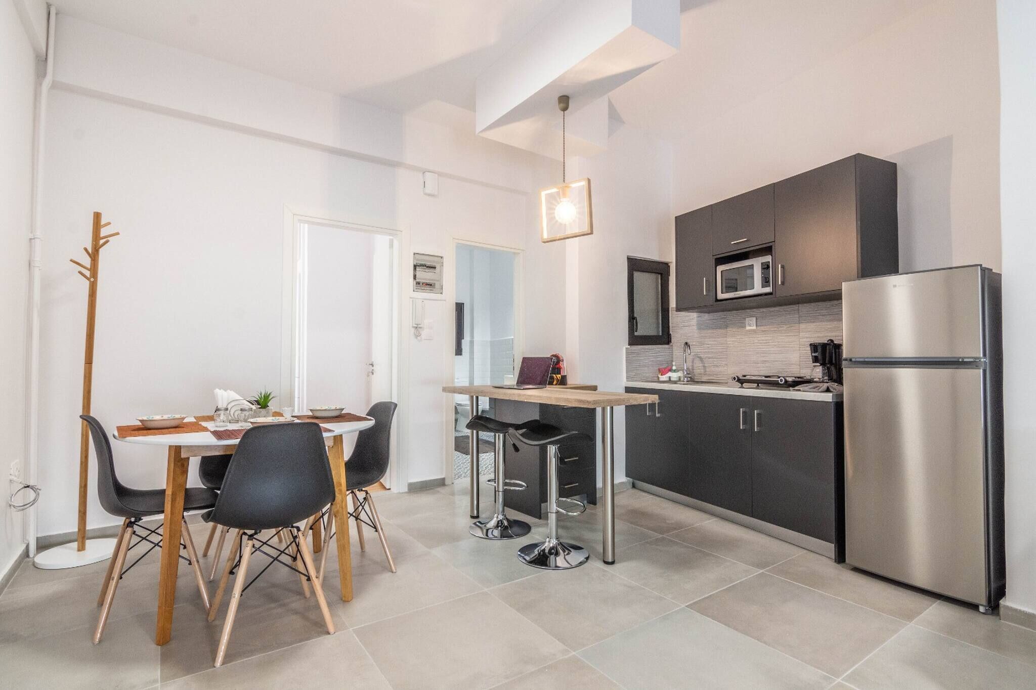 Una cocina moderna con armarios oscuros, un refrigerador de acero inoxidable y una zona de comedor con mesa y sillas.