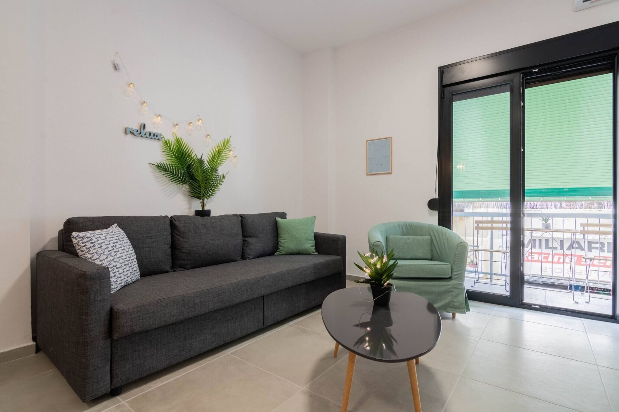 Una sala de estar moderna con un sofá gris, un sillón verde, una mesita negra y una planta en maceta.