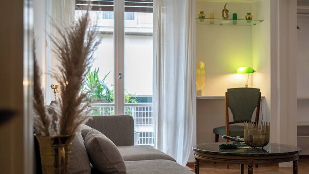 A living room with a sofa, a round table, a chair, and a vase with dried plants.