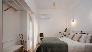 A bedroom with a bed, bedside table, hanging clothes rack, and a potted plant.