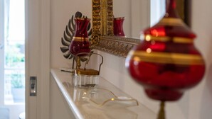 A hallway with a white wall, a large ornate mirror, and a red vase on a white console table.