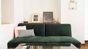 A green sofa with a patterned pillow, a glass coffee table with remote controls, and framed artwork on the wall. - Athens' Best Location! ~Stunning & Spacious Studio (Athens)