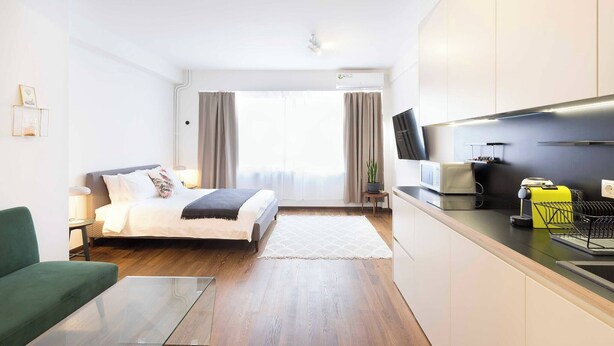 A compact hotel room with a bed, a green sofa, a small table, a kitchenette, and a TV. - Athens' Best Location! ~Stunning & Spacious Studio (Athens)