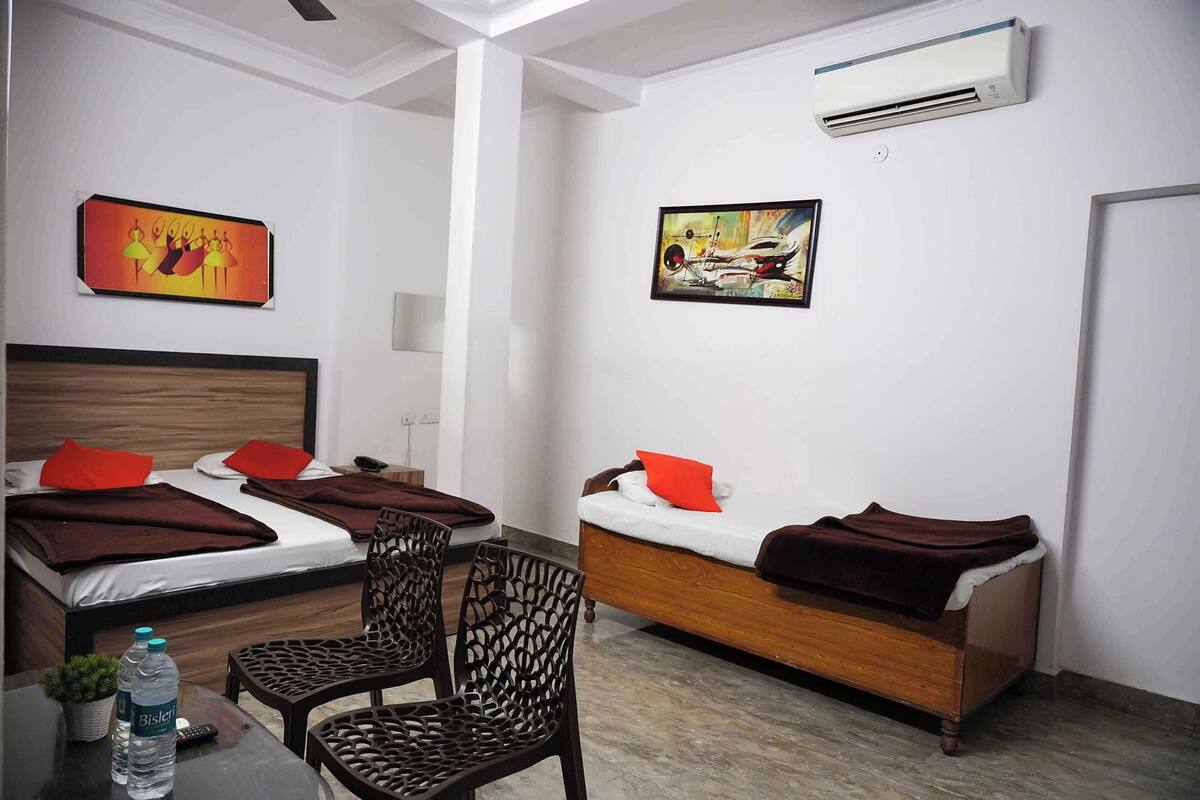 A hotel room with two beds, a sofa, a chair, a table with a water bottle, and two paintings on the walls.