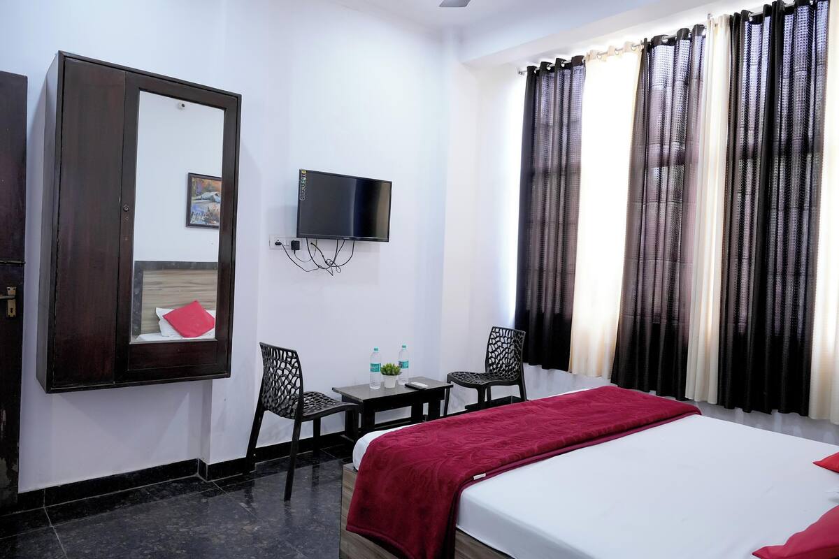 A hotel room with a bed, a desk, two chairs, a TV, and a window with curtains.