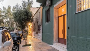 Une rue étroite, bordée de voitures garées, et un immeuble à la façade verte portant le numéro « 76 ».
