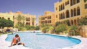 A swimming pool with a clear blue water, surrounded by a building with arches and a stone wall.