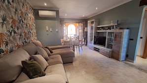 Una sala de estar con un sofá modular, un mueble para la TV y un comedor con mesa y sillas.