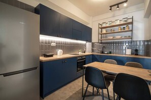 Eine moderne Küche mit dunkelblauen Schränken, einem Edelstahlkühlschrank, einem Holzesstisch und einem eingebauten Backofen.