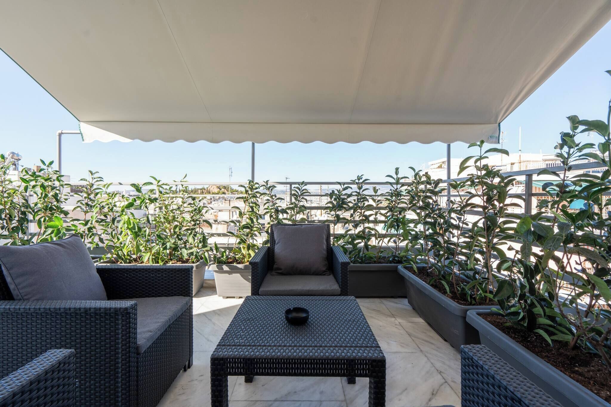 A rooftop patio with wicker furniture, potted plants, and a canopy.