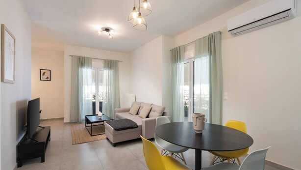 A modern living room with a sofa, coffee table, and dining table with chairs. There is a TV stand, an air conditioner, and a window with curtains. - Prime 3BR Exarcheia Penthouse | Huge Terrace (Athens)