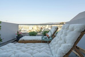 Un balcón con cama, una mesita con una bebida y plantas en macetas.