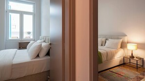 Un dormitorio con dos camas, una mesita de noche, una lámpara y una ventana.