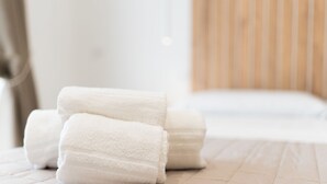 A neatly arranged stack of white towels on a wooden floor in a room with a striped wall and a white bed. - Olivia's Home By DomusExtra (Naples)