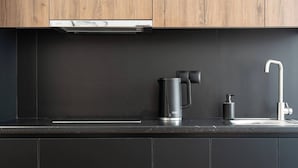 A modern kitchen with dark cabinetry, a built-in oven, a coffee maker, and a faucet.