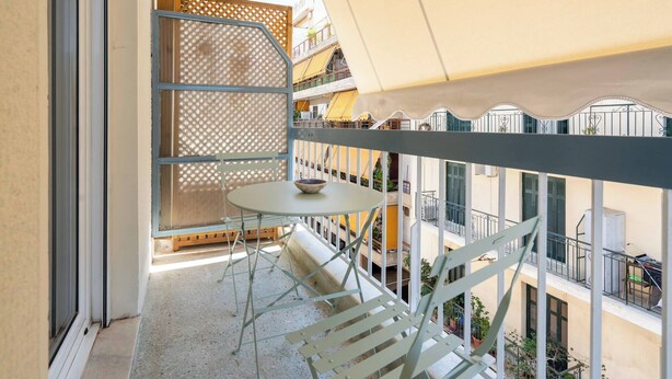 A balcony with a table and chairs, a view of neighboring buildings, and a lattice partition. - Bright 2BR Apartment By Metro Near Acropolis (Athens)