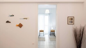 A hallway with a door leading to a room with a bed and a nightstand. There are wall decorations and a plant on the right side. - Bright 2BR Apartment By Metro Near Acropolis (Athens)