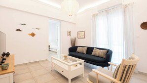 A modern living room with a dark blue sofa, a white coffee table, and a wooden chair. - Bright 2BR Apartment By Metro Near Acropolis (Athens)