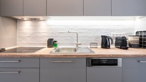 Een moderne keuken met grijze kastjes, een houten aanrechtblad, een roestvrijstalen spoelbak, een koffiezetapparaat en een vaatwasser.