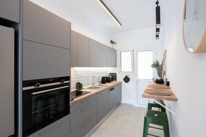 A modern kitchen with grey cabinets, a built-in oven, a wooden countertop, and a green stool.