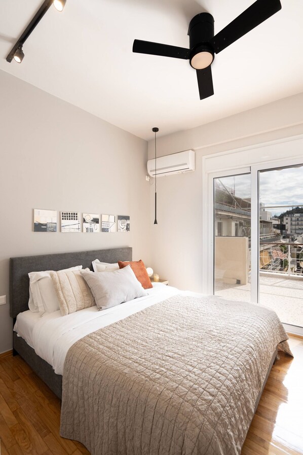A modern bedroom with a large bed, a ceiling fan, and a city view through the sliding glass door.
