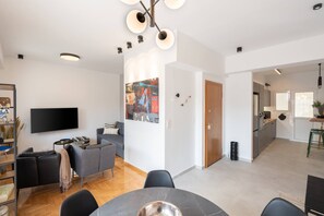 A modern living room with a flat-screen TV, grey sofa, and a dining area with a round table.
