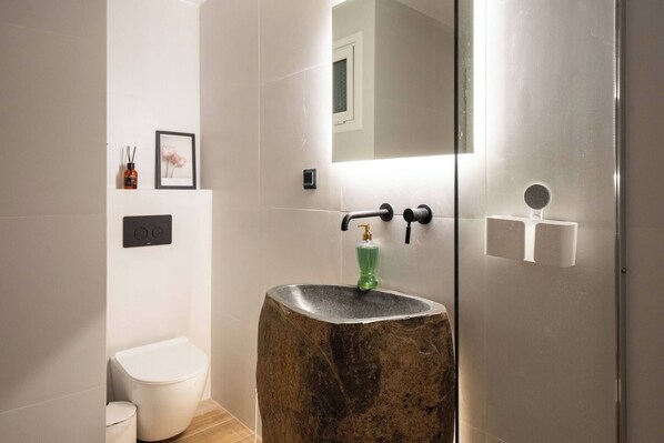 A bathroom with a stone sink, a toilet, a framed picture, and a mirror.