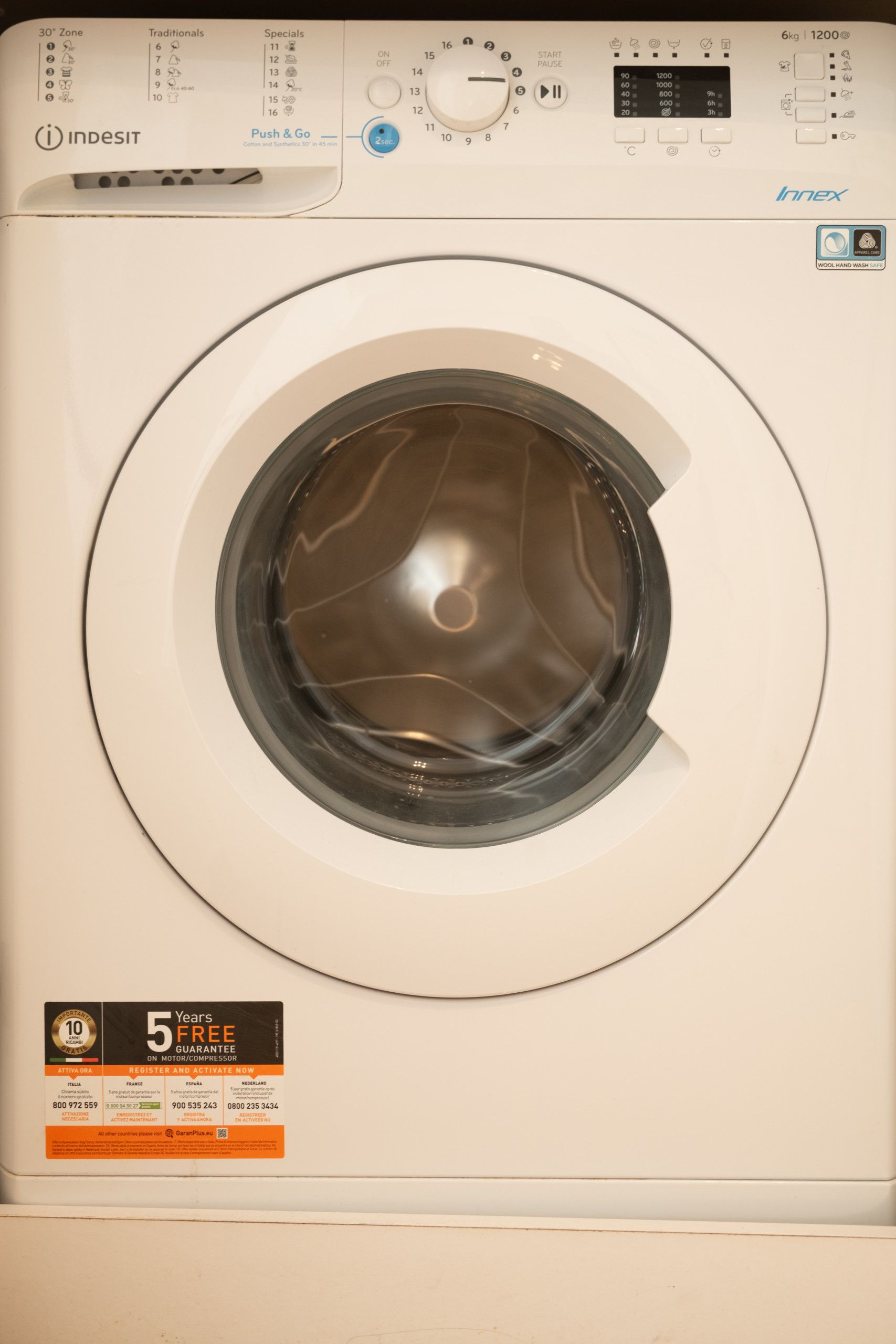 A front view of a white washing machine with a digital display, control panel, and a 5-year free guarantee sticker.