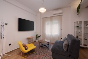 A modern living room with a flat-screen TV, a sofa, a yellow chair, a small table, and a potted plant. - 1BR Stylish Apt 20 Minutes from Acropolis (Athens)