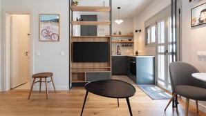 Une cuisine moderne dotée d’un téléviseur encastré, d’étagères en bois et d’un coin repas avec des chaises.