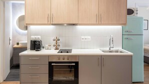 A compact kitchen with wooden cabinets, a built-in oven, a sink, and a teal refrigerator.