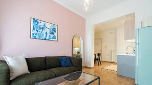 A living room with a sofa, a glass coffee table, a kitchen area with a fridge, and a dining area with chairs.
