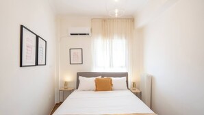 A bedroom with a bed, bedside tables, an air conditioner, a window with curtains, and framed pictures on the wall.